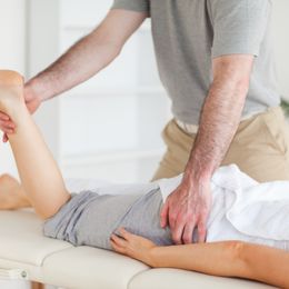 A chiropractor stretches a female customer's leg in his surgery